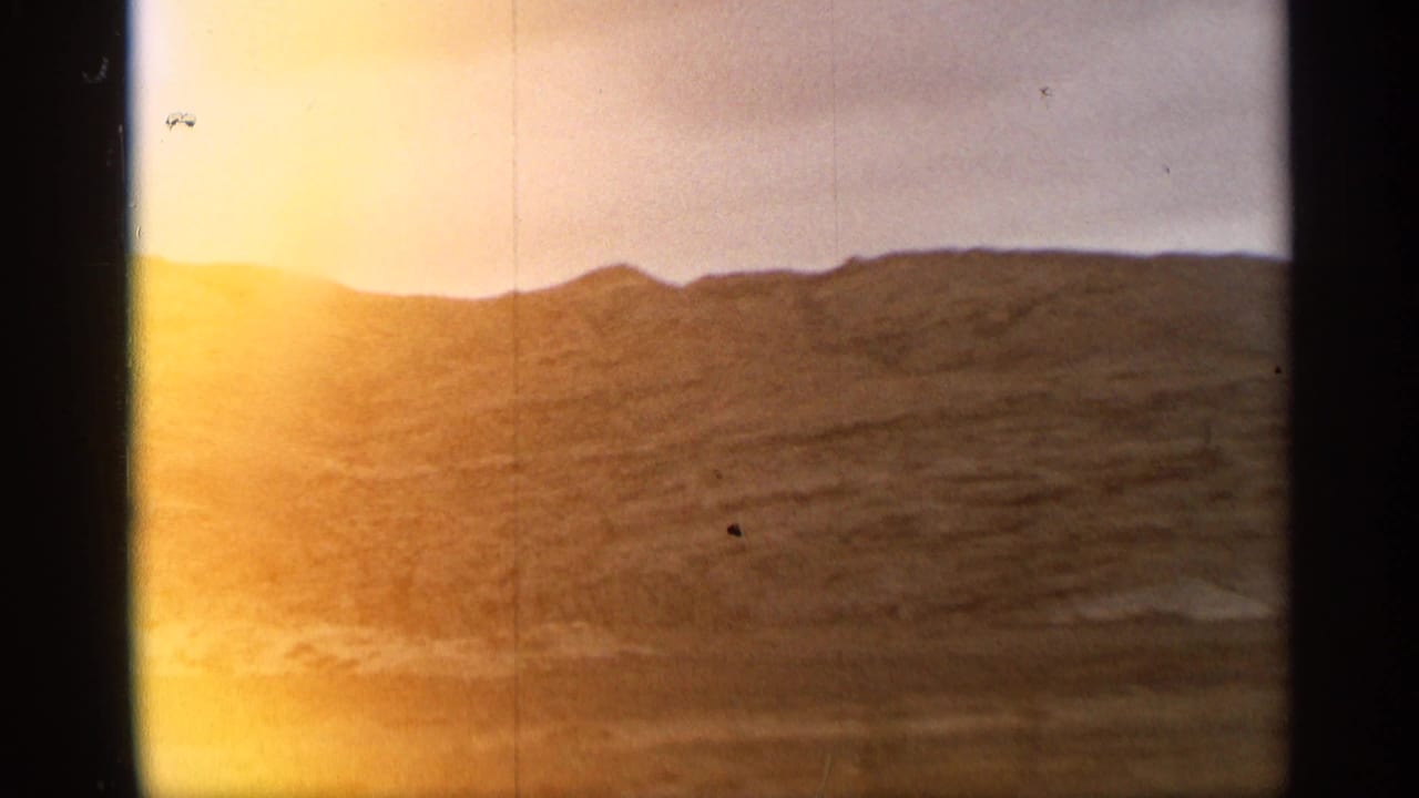 Sunlit rolling hills under a bright sky with visible 8mm film edges.