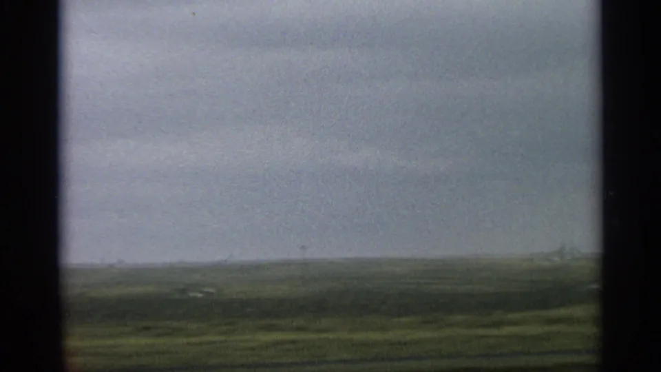 1959 Arizona home-movie frame with low open plain, distant hills, pale overcast sky, and visible film grain.