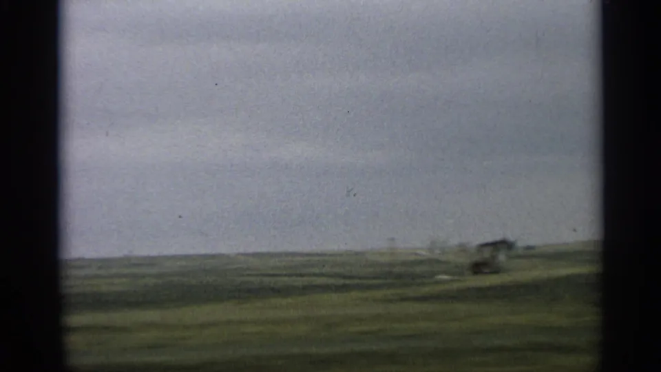 1959 Arizona road-trip frame showing open plains, distant hills, utility poles, and a small vehicle-like shape near the right edge.