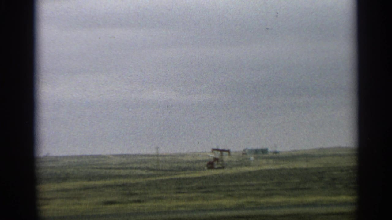 Distant oil pump jack in a green field beneath a cloudy sky.