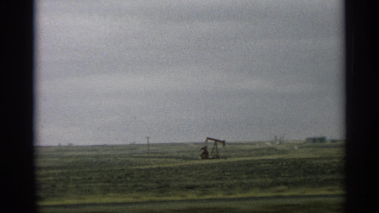 Oil pump jack on the horizon with open field and utility poles.