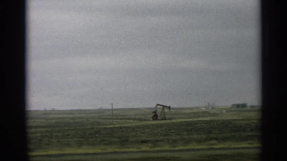 1959 Arizona roadside view of a pump jack on the horizon, with open green field and cloudy sky.