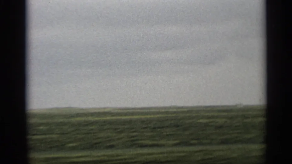 1959 Arizona 8mm roadside view across open green field toward a low horizon under cloudy sky.