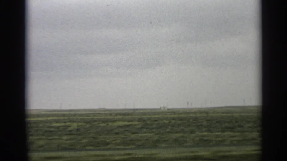1959 Arizona home-movie view of a broad green desert plain under a pale overcast sky, with soft motion blur from travel.