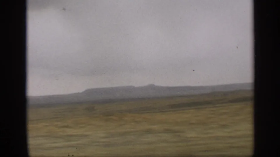Distant Arizona mountain ridge appears beyond muted desert fields in a 1959 8mm travel view from a moving vehicle.