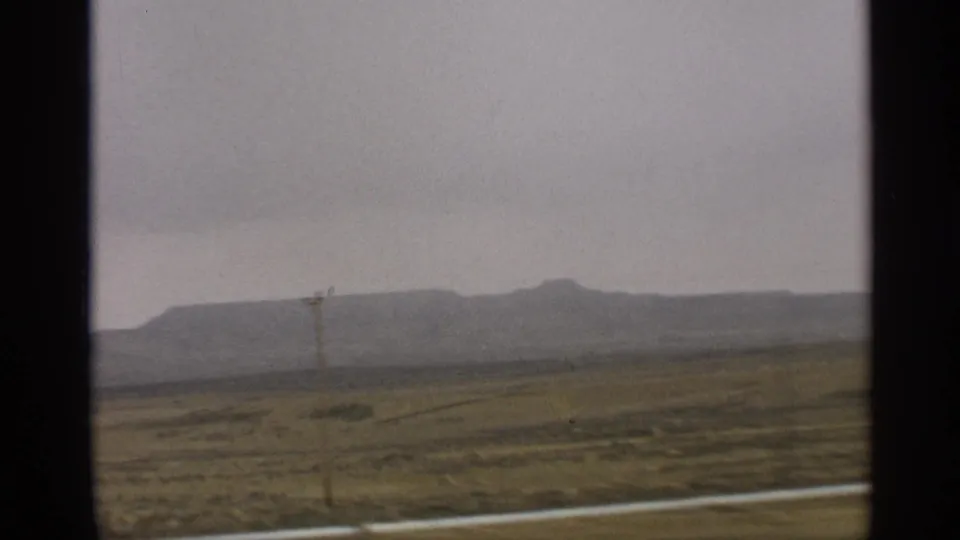 A roadside power pole passes through the frame as desert fields and a hazy Arizona ridge recede in the background.