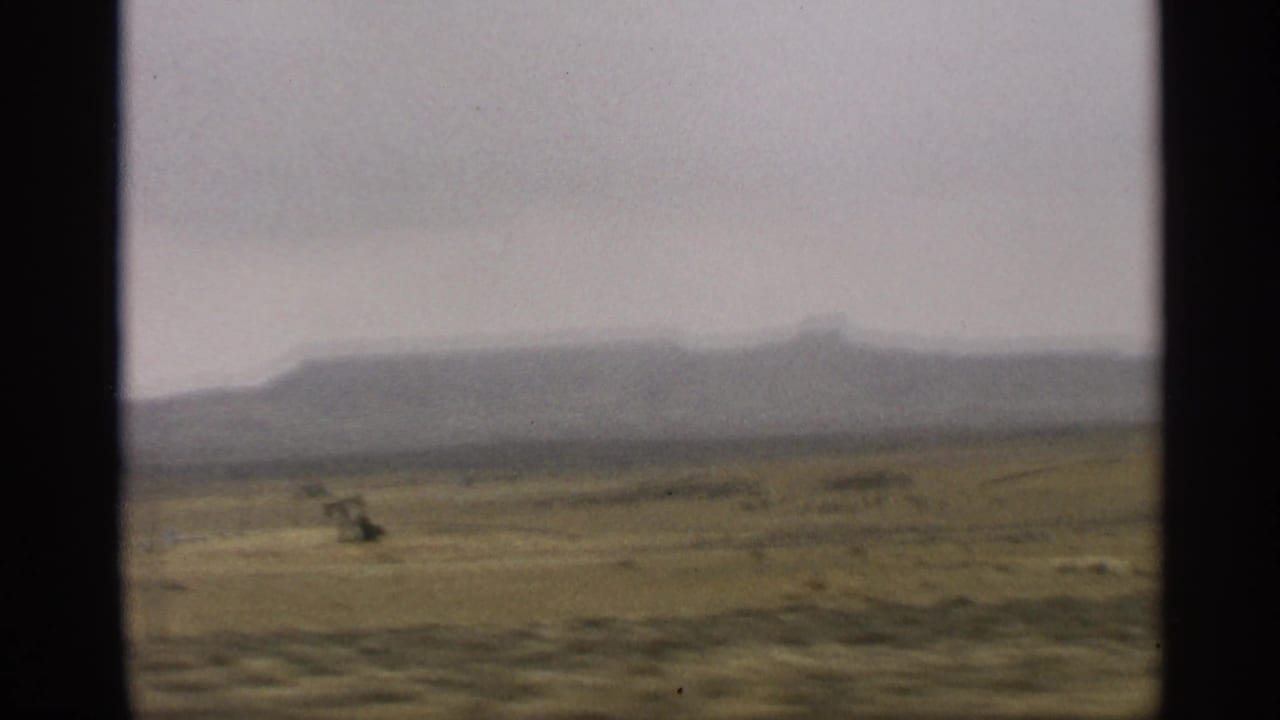 Flat desert landscape with distant mesas seen through a car window.