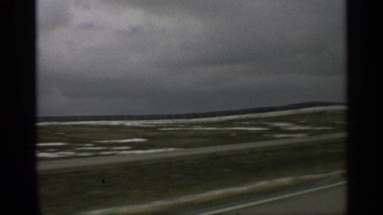 Arizona road-travel view showing open desert, pale snow or wet patches, a blurred roadside, and a dark cloudy sky.