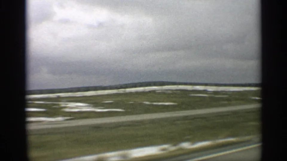 Moving-car view across Arizona desert flats, with scattered pale patches, a blurred road foreground, and heavy cloud cover.