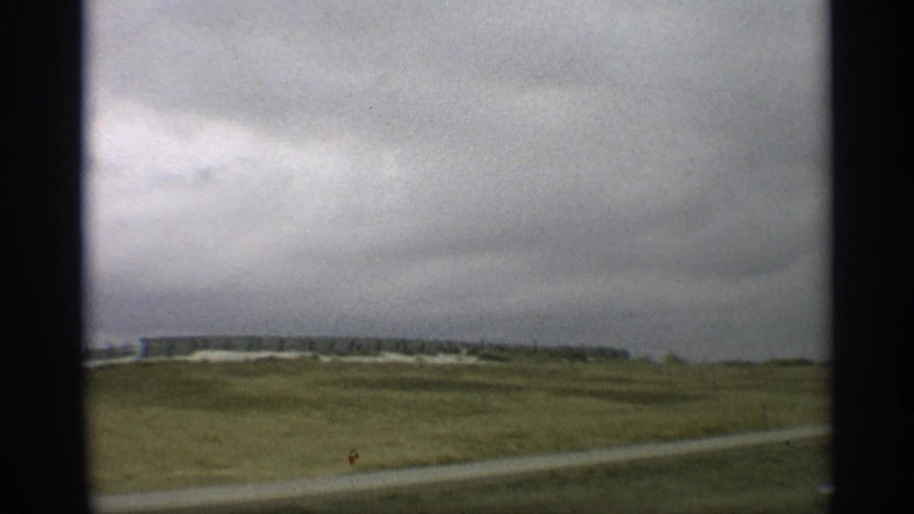 Low rural building beyond open grassland and a roadside curve.