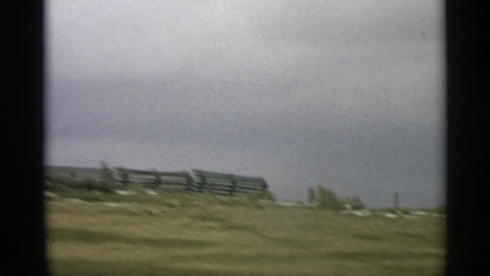 1959 Arizona 8mm frame showing a blurred fence line and dry open ground from a moving vehicle.