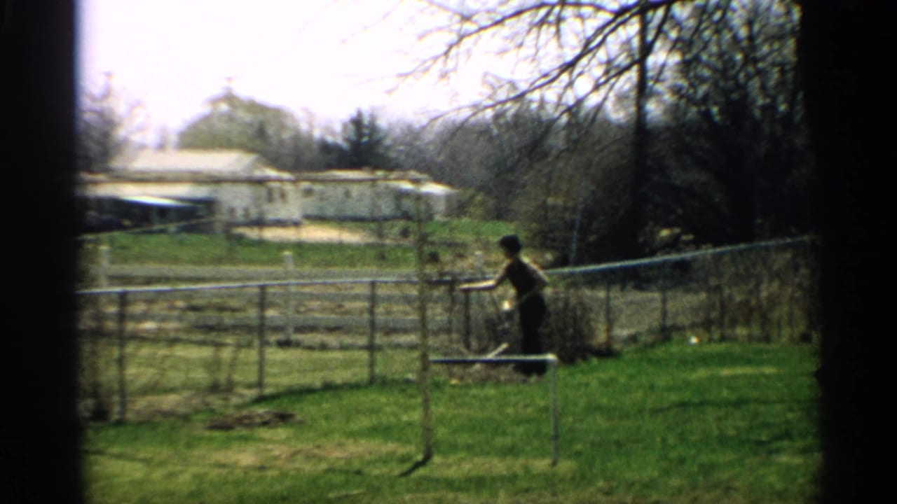 Woman standing in a backyard near a chain-link fence with lawn, trees, and a house beyond.