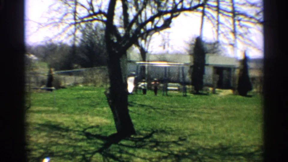 The final frame shows the person small in the distance near the fence, with the backyard lawn, tree shadows, and light structures behind.