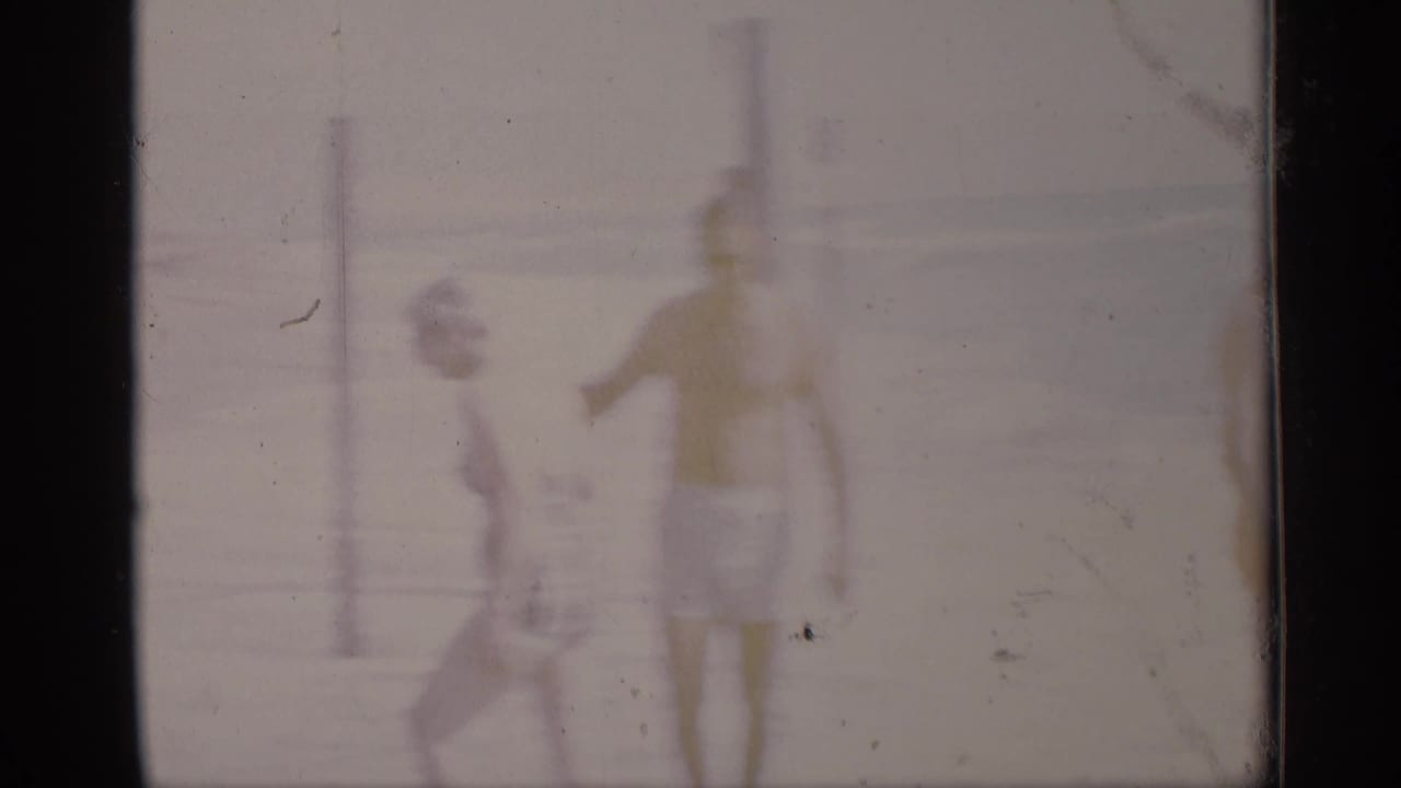 Two beachgoers in swimsuits near posts, seen through soft faded exposure.