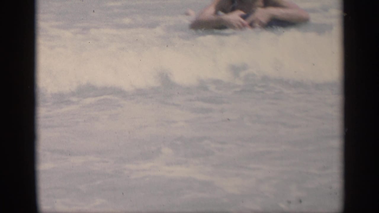 Swimmers float in shallow ocean water, partly obscured by soft focus and film gate edges.