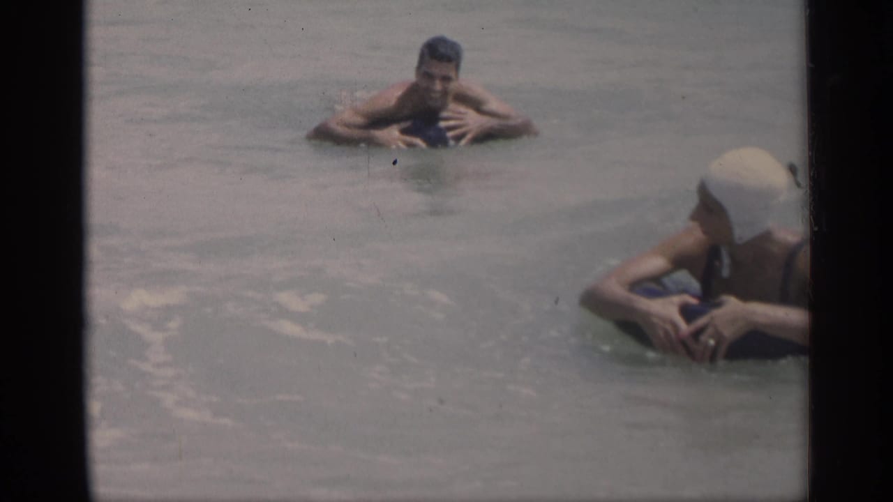 Two swimmers in the ocean, including a woman in a white swim cap near the right edge.