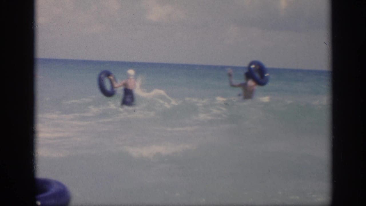 Adults play in ocean waves with blue inflatable rings.