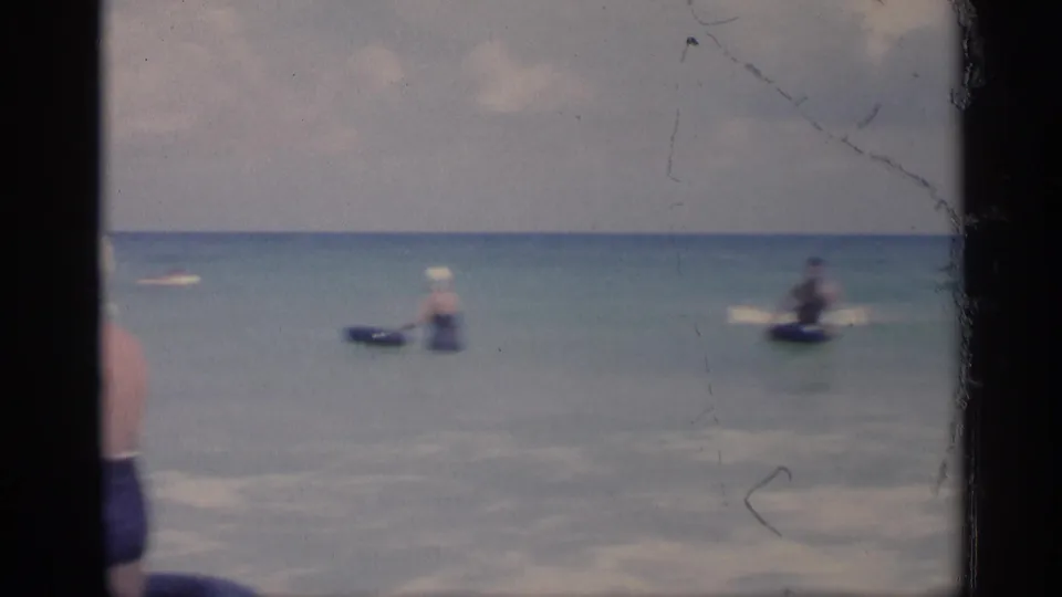 1959 California beach home-movie frame showing shallow surf, distant swimmers, a horizon line, and visible 8mm film borders.