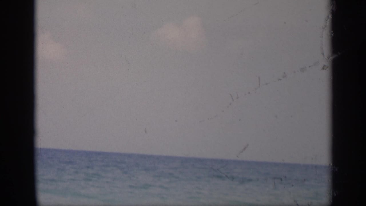 1959 California 8mm frame showing a calm ocean horizon and pale sky, bordered by dark vertical film edges.