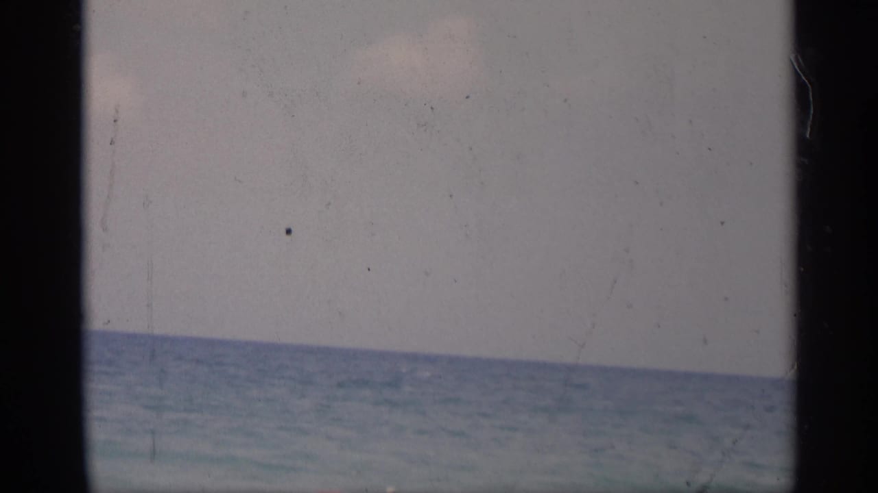 Calm ocean and pale sky seen through dark film-frame borders.