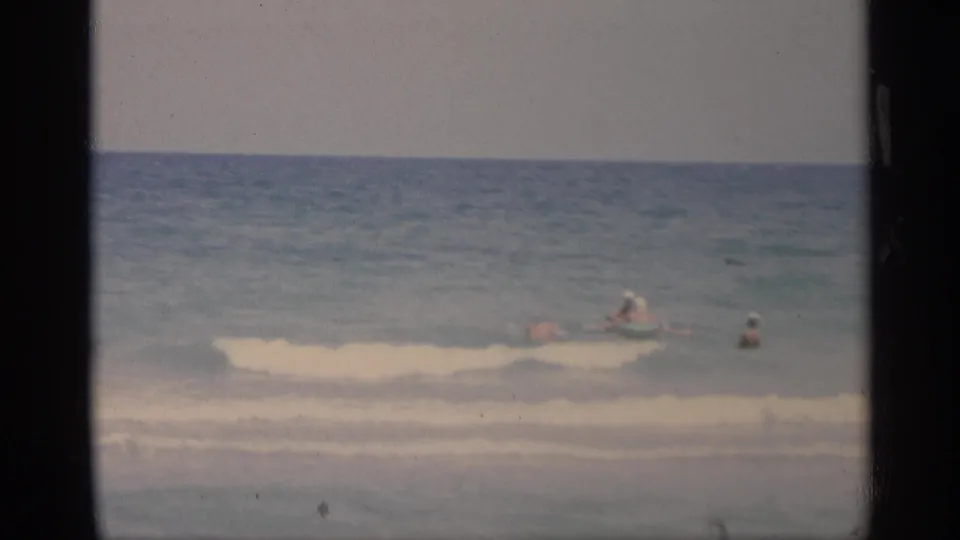 Swimmers play in the surf off a California beach in 1959, seen from shore in soft 8mm home-movie color.