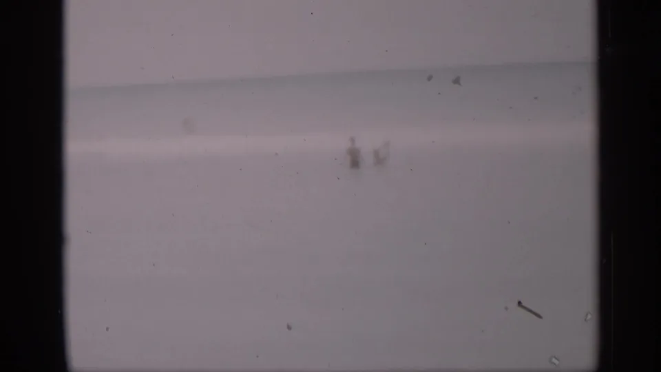 Distant California shoreline view with a few small figures in the water, rendered with faded color and soft 8mm texture.