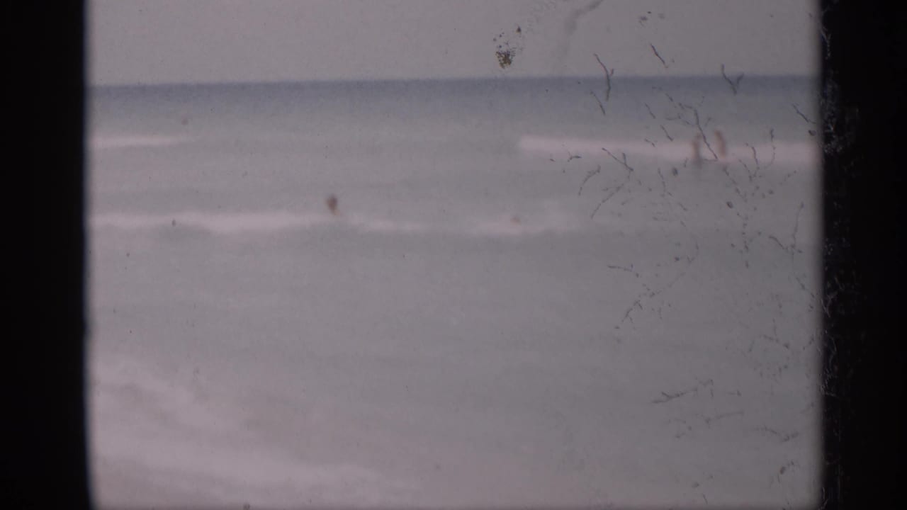 Soft 8mm beach frame with surf and a distant figure near the water.