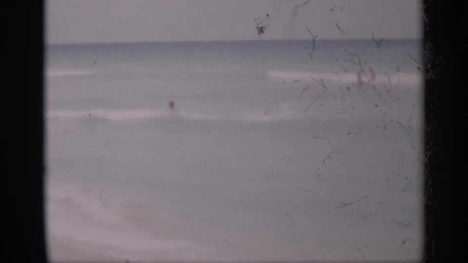 1959 California 8mm beach view with pale surf, sand, and a small distant figure near the ocean.