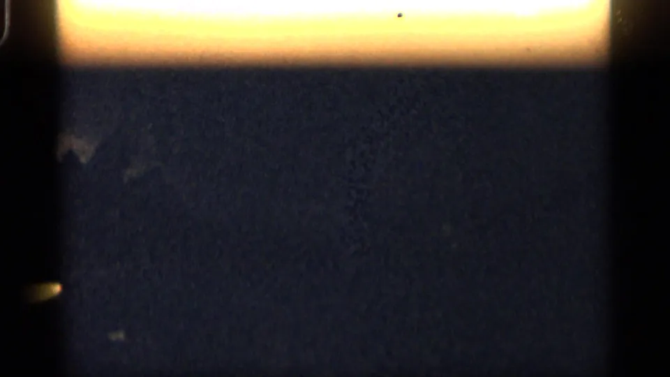 A mostly dark, underexposed transitional frame shows film edge and faint interior shapes with no clear action visible.