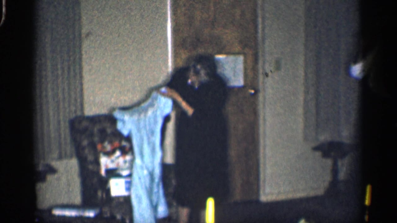 Woman in a dark dress holds up a light blue garment near a door and chair.