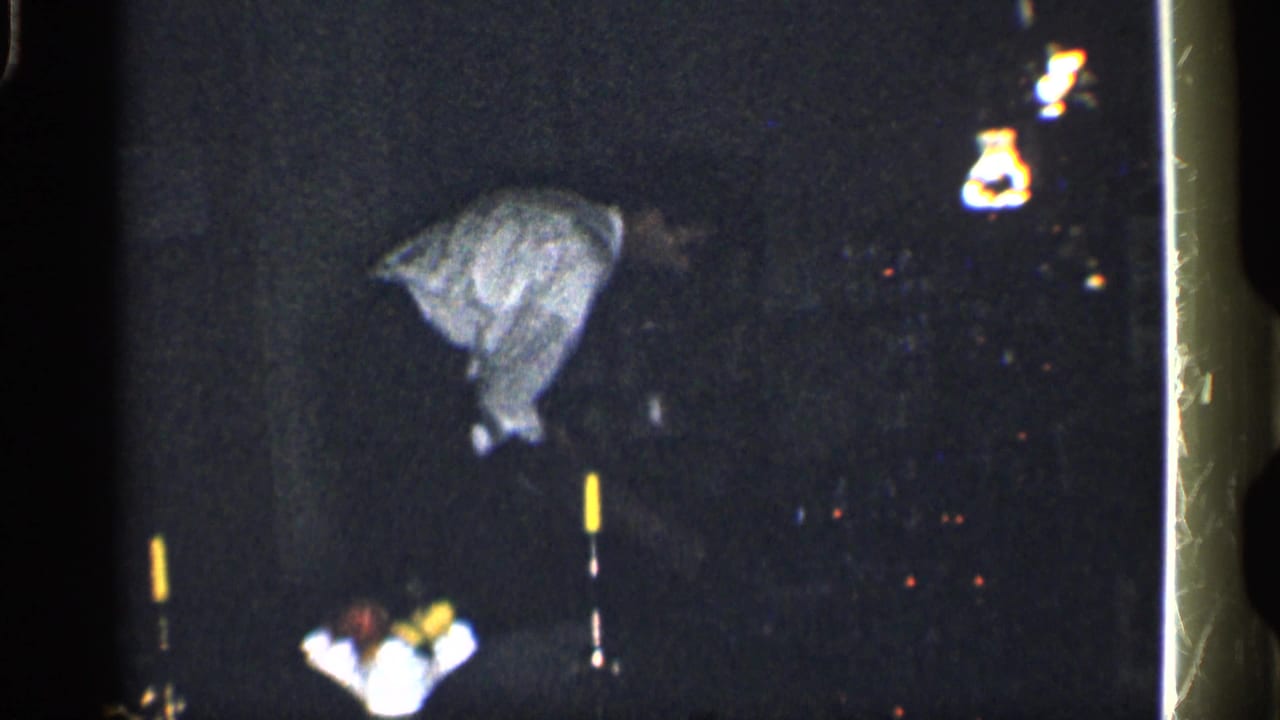 Man bending in a dark room with a yellow-tipped pole in the foreground.