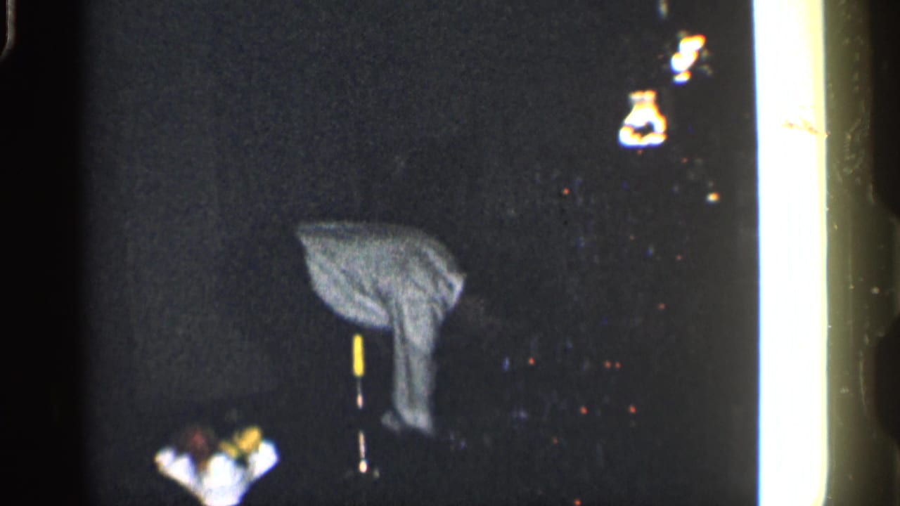 Man bent over in a dark interior beside a yellow-tipped vertical pole.