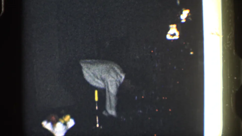 Adult man in a light shirt appears bent over in a dark 1959 California home-movie interior with film-edge flare.