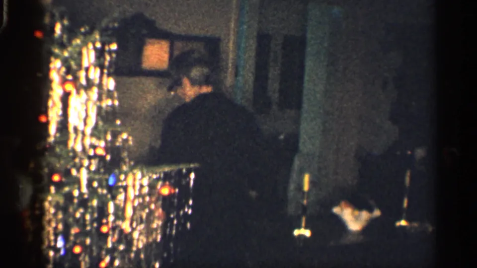 Adult man seen from behind near a reflective tinsel Christmas tree inside a 1959 California holiday home interior.