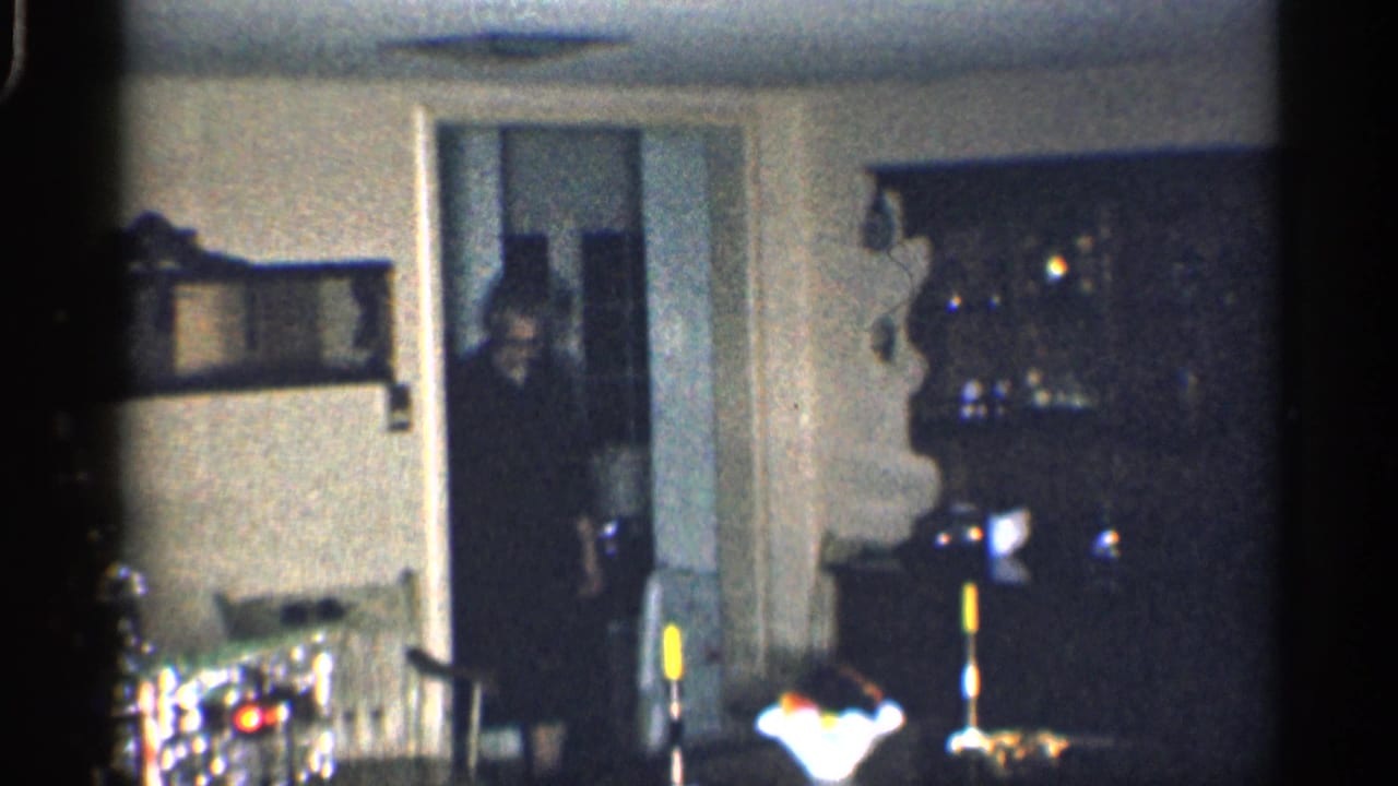 Man partly visible in a doorway beside a china cabinet in a dim living room.