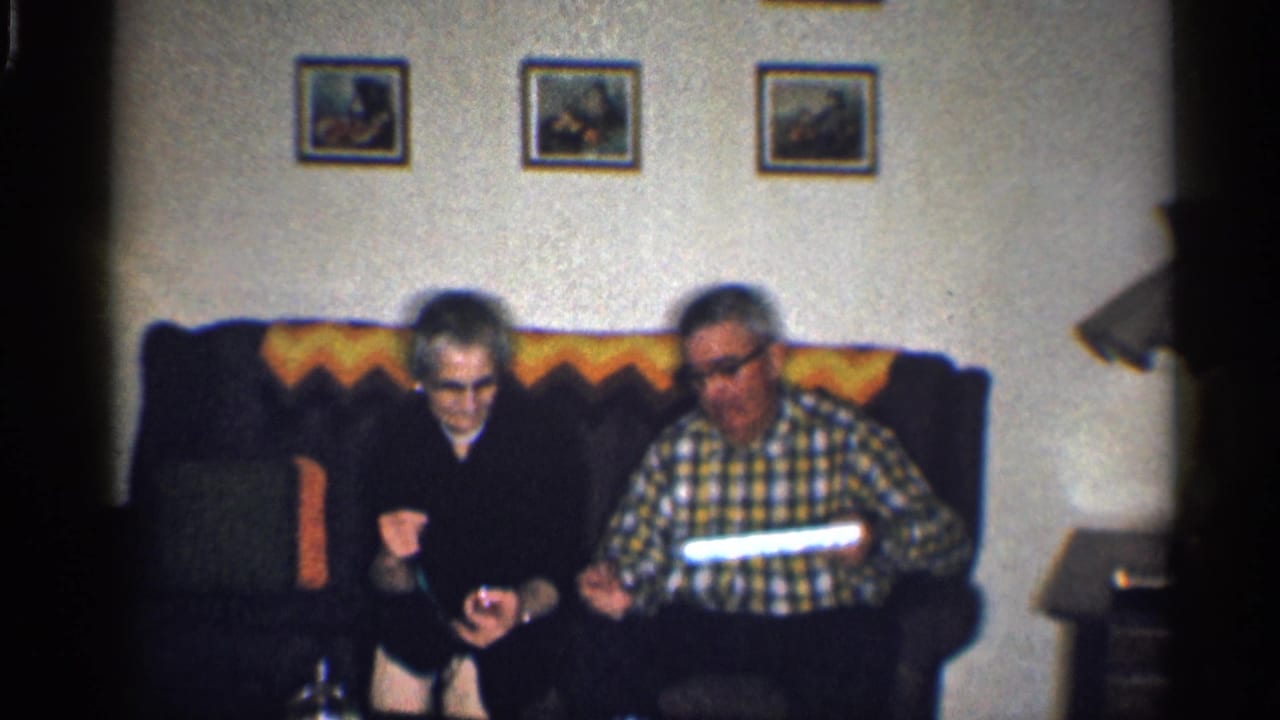Elderly woman and man sit on a dark sofa with gifts in their hands.