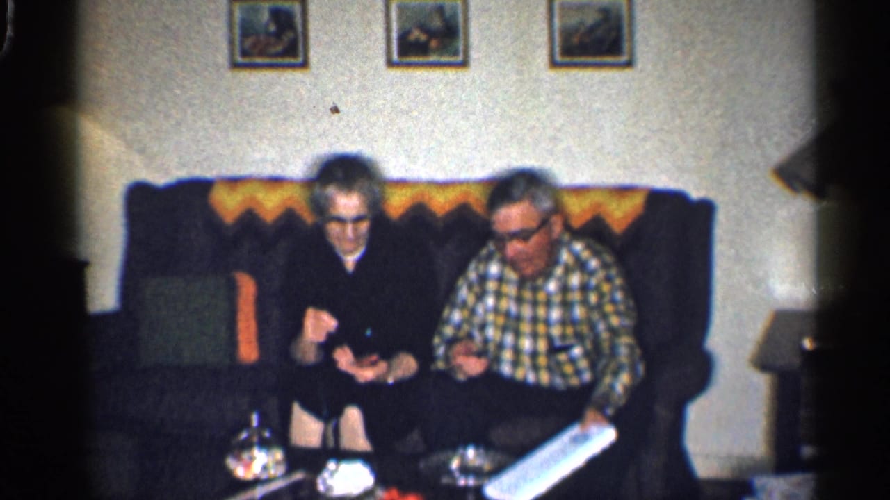 The couple sits on the sofa as the man holds a long white box.