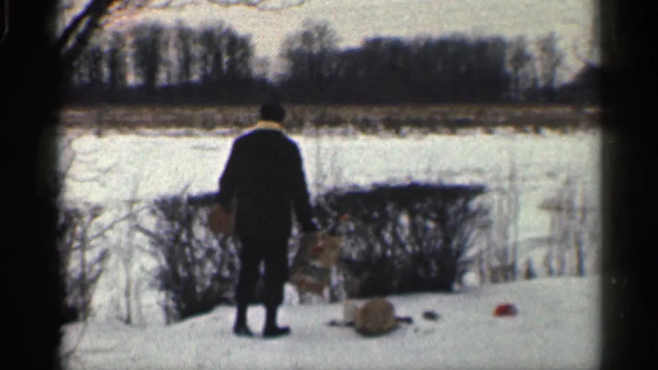 Seen from behind, the man stands near shrubs and dogs at the edge of a snowy California yard, with open ground or water beyond.