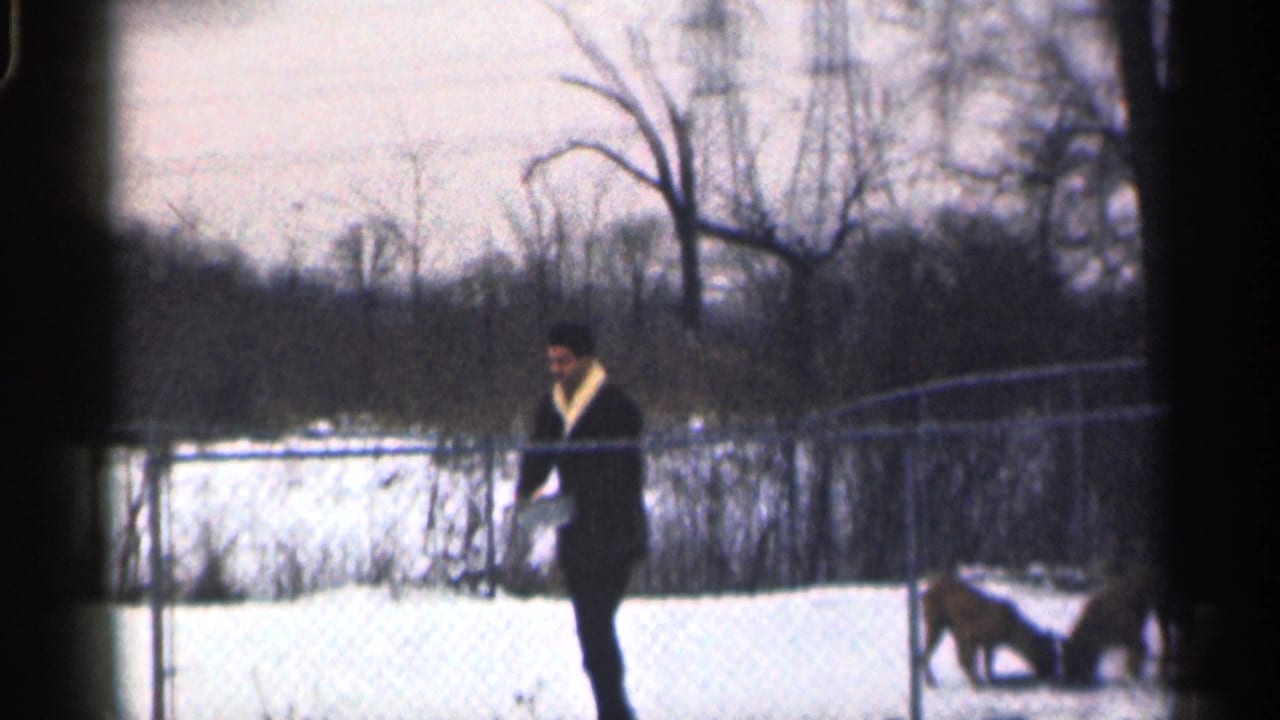 Man in dark winter clothing walks along a snowy fenced yard.