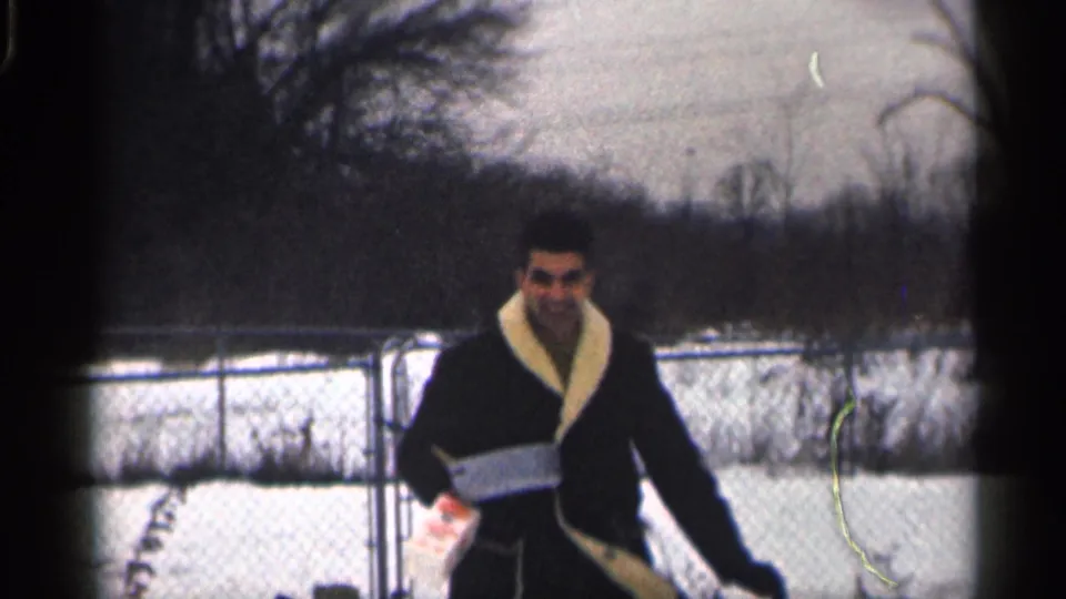 The man smiles toward the camera while holding a small package in a snowy California yard in 1959.