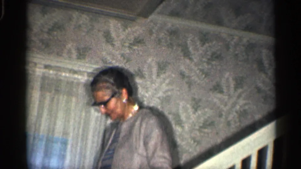 The woman descends the staircase in a private California home, with sheer curtains and patterned wallpaper visible behind her.