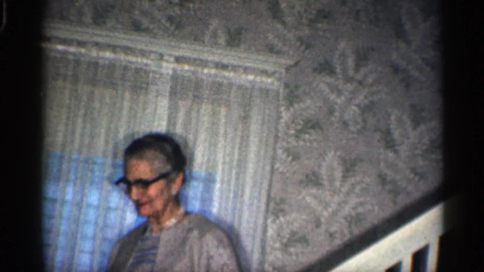 Near the bottom of the visible stair section, the woman appears to smile beside the railing and sheer-curtained window.