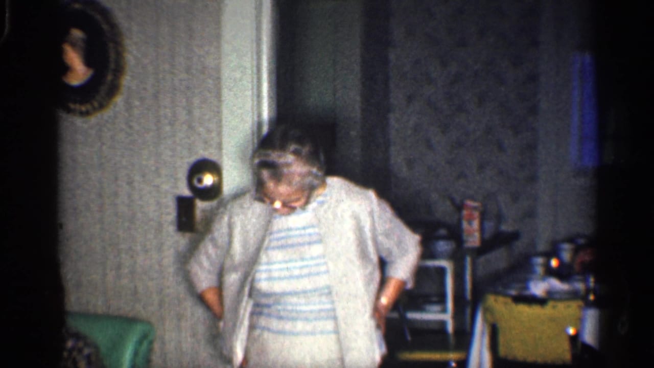 Woman in glasses stands barefoot in a room, looking down with her hands near her pockets.