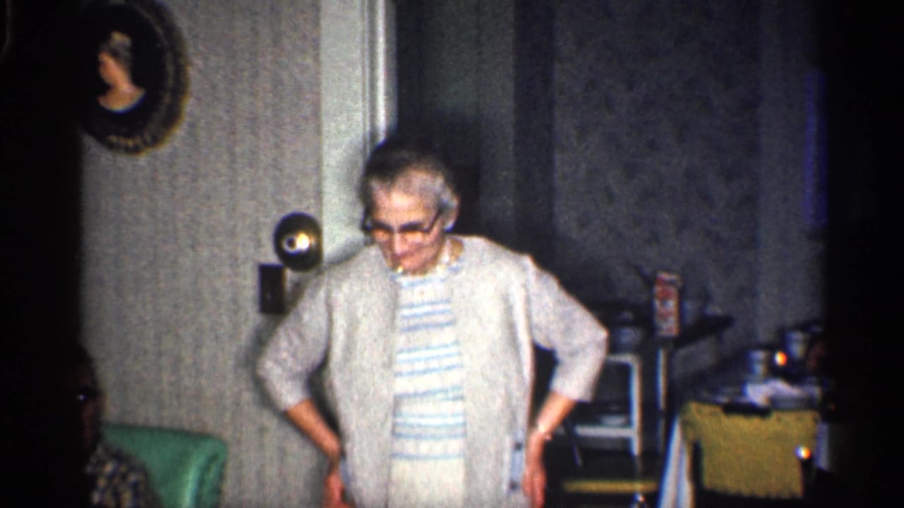 Woman in a light cardigan faces forward with hands at her sides in a domestic room.