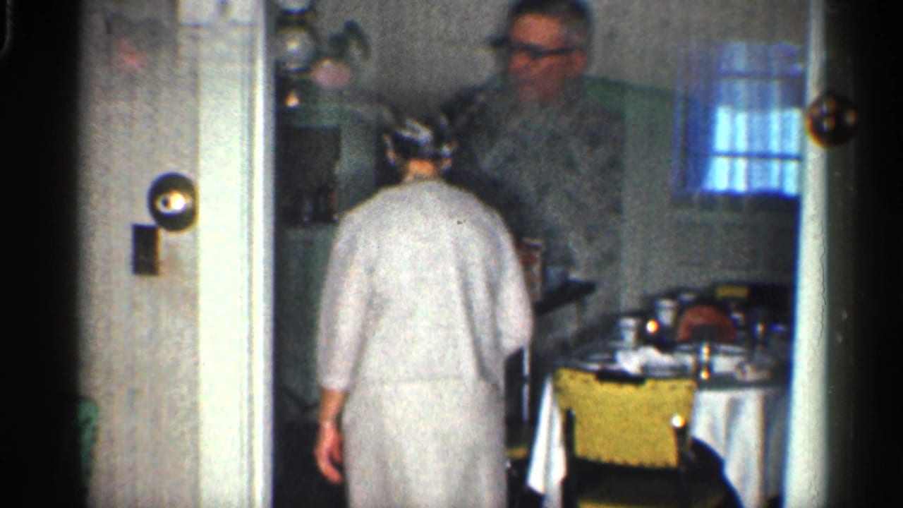 Woman seen from behind entering a small dining area while a man is visible near the table.