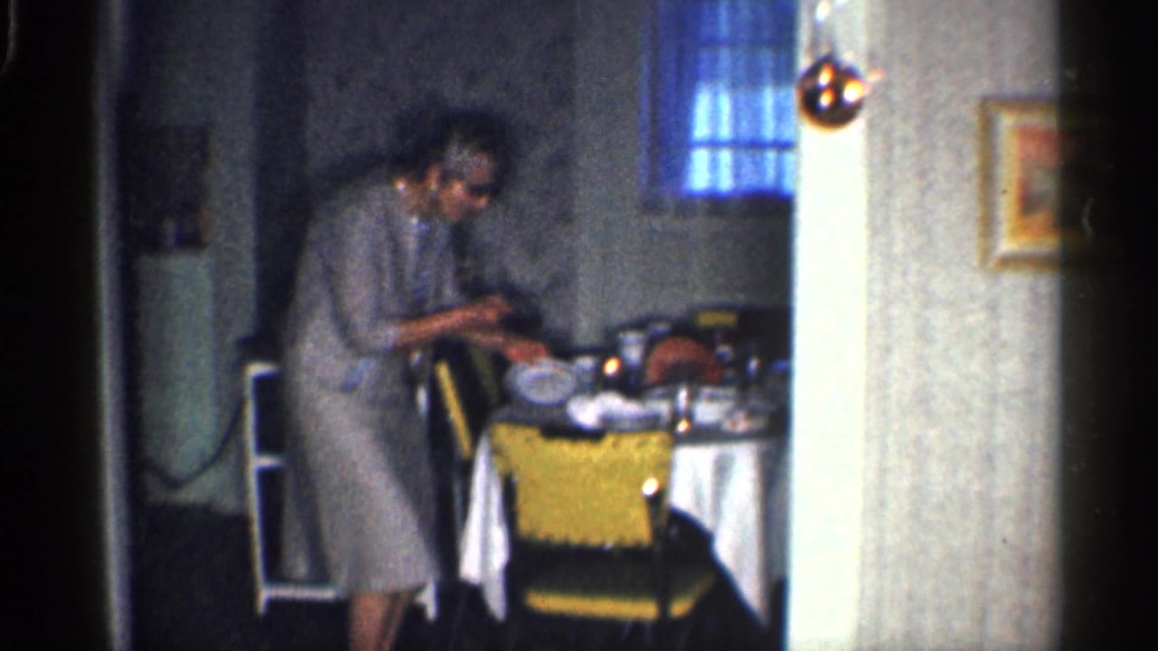 Woman in sunglasses stands by a kitchen table viewed through a doorway.
