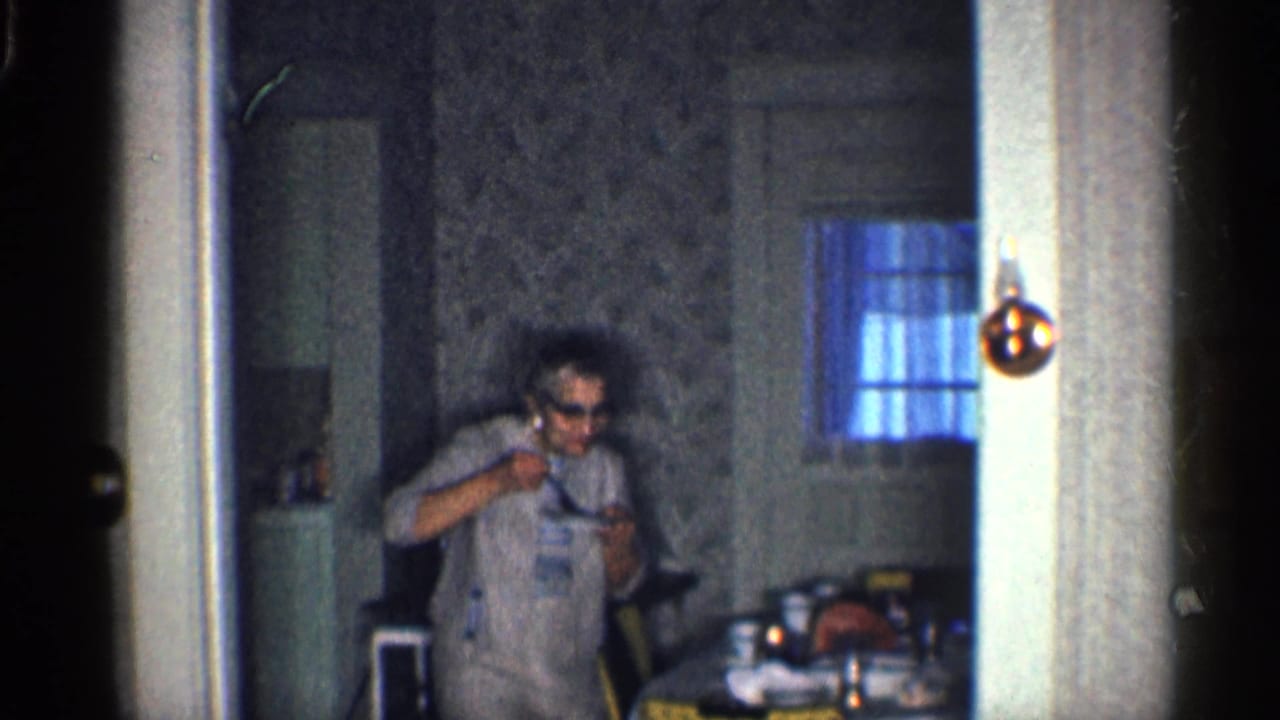 Woman in sunglasses gestures with one hand near a kitchen table.