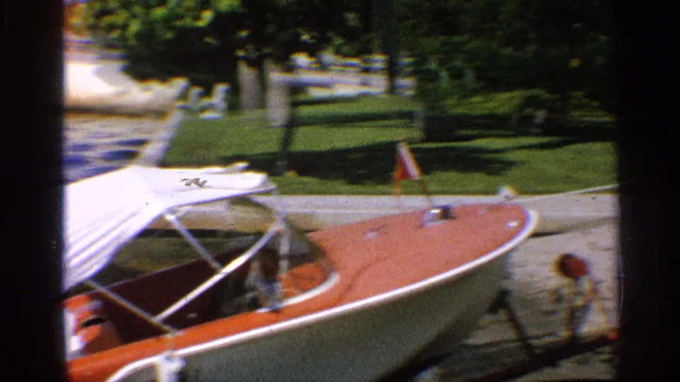 The red-and-white speedboat is positioned at the water's edge, with trees and a grassy shoreline visible in the background.