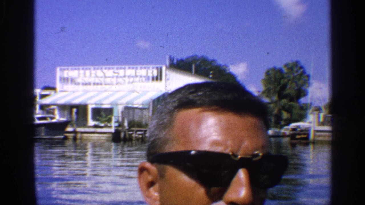 Man in sunglasses in front of marina buildings and a Chrysler sign.