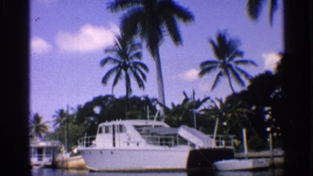 1959 California 8mm frame showing a white cabin boat at a dock with palm trees, calm water, and dark film-frame edges.